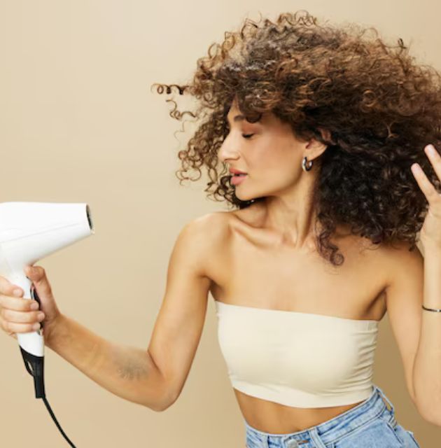 "Person using a microfiber towel to gently squeeze excess water from curly hair, reducing frizz."